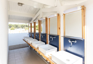 Espace de lavage extérieur lumineux et moderne avec plusieurs lavabos et miroirs dans un site de glamping.