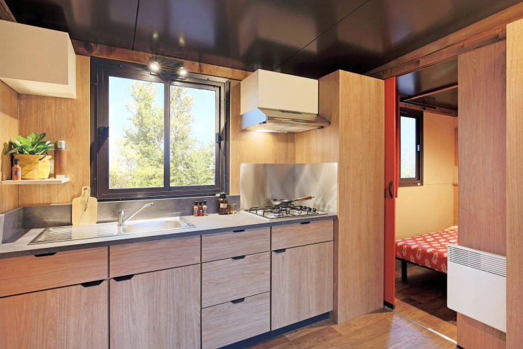 Modern kitchen in a safari tent at Huttopia Ars-en-Ré, France, with wooden cabinets and gas stove.