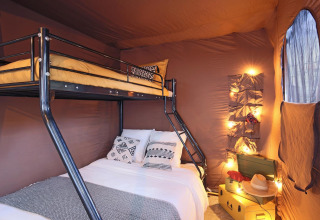 Interior de la tienda safari Arizona en Huttopia Ars-en-Ré, Francia, con litera y luces decorativas.