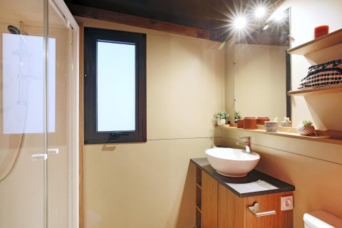 Bagno moderno nella tenda safari Arizona di Huttopia Ars-en-Ré, con doccia, lavabo e decorazioni calde.