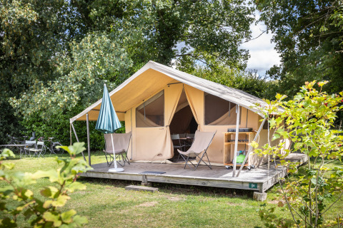 Tente Safari Tent Classic avec terrasse couverte et chaises, entourée de verdure sur un camping ensoleillé.