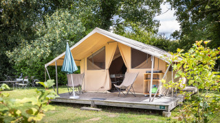 Tienda Safari Tent Classic con terraza cubierta y sillas rodeada de vegetación en un camping soleado.