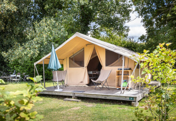 Tente Safari Tent Classic avec terrasse couverte et chaises, entourée de verdure sur un camping ensoleillé.