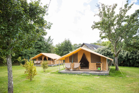 Dos tiendas safari sobre césped verde, rodeadas de árboles en Huttopia Calvados - Normandie en Francia.