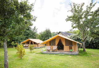 Deux tentes safari sur une pelouse verte, entourées d’arbres à Huttopia Calvados - Normandie en France.