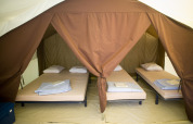 Vista interior de una tienda safari con cuatro camas individuales, sábanas y almohadas en Huttopia Calvados, Francia.
