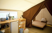Vista interior de una tienda safari con zona de cocina y cama en Huttopia Calvados - Normandie, Francia.