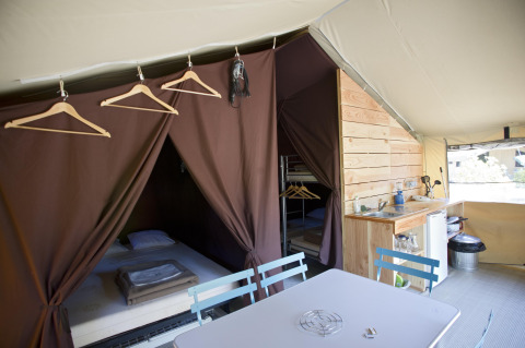 Interior de la tienda safari Tent Sweet en Huttopia Calvados - Normandie, Francia, con camas y cocina pequeña.