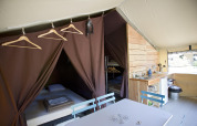 Interior de la tienda safari Tent Sweet en Huttopia Calvados - Normandie, Francia, con camas y cocina pequeña.