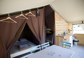Binnenzicht van de Tent Sweet safaritent bij Huttopia Calvados - Normandië, Frankrijk, met bedden en keuken.