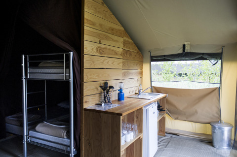 Interieur van een safaritent met keukenblok, koelkast en stapelbed bij Huttopia Calvados, Normandië.