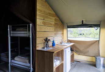 Interieur van een safaritent met keukenblok, koelkast en stapelbed bij Huttopia Calvados, Normandië.