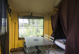 Interior de una tienda safari con mesa de comedor, sillas y cama en Tent Sweet, Huttopia Calvados - Normandie, Francia.