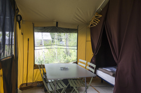 Interior de una tienda safari con mesa de comedor, sillas y cama en Tent Sweet, Huttopia Calvados - Normandie, Francia.