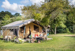Familia relajándose delante de una tienda safari en Huttopia Calvados - Normandie, Francia, en la naturaleza.