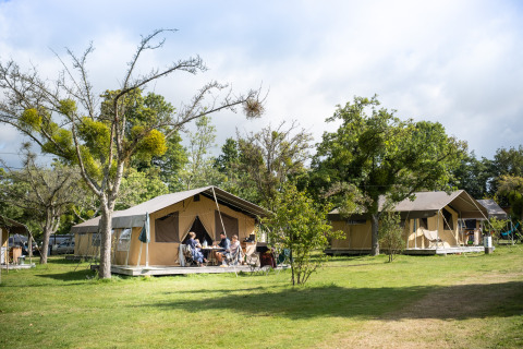Tiendas safari en Huttopia Calvados - Normandía, Francia, con personas relajándose al aire libre en el césped.