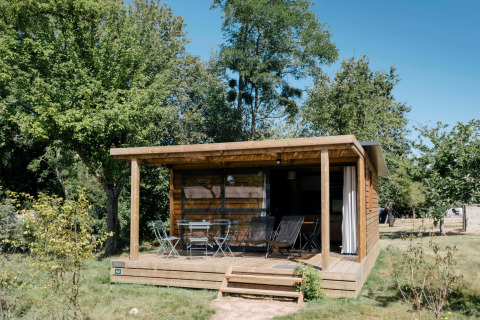 Træchalet Evasion med overdækket terrasse og havemøbler, omgivet af grønne træer og natur.
