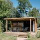 Træchalet Evasion med overdækket terrasse og havemøbler, omgivet af grønne træer og natur.