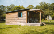 Chalet de madera con terraza cubierta y muebles de exterior en césped en Huttopia Calvados - Normandie, Francia.