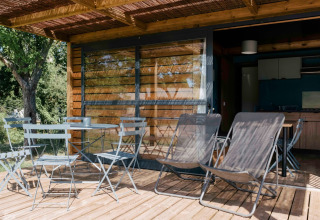 Terraza exterior del Chalet Evasion en Huttopia Calvados - Normandie, con mesas, sillas y tumbonas.