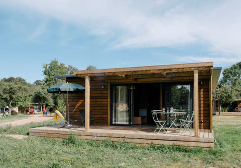 Das Chalet Portland von außen mit überdachter Terrasse, Gartenmöbeln und grüner Umgebung.