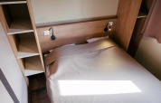 Cama acogedora con estanterías de madera en Chalet Portland en Huttopia Calvados - Normandie, Francia, decoración simple.