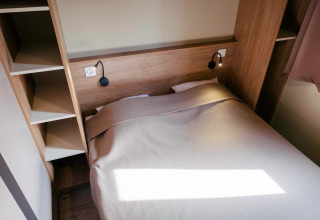 Cama acogedora con estanterías de madera en Chalet Portland en Huttopia Calvados - Normandie, Francia, decoración simple.