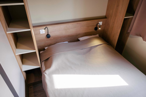 Gemütliches Bett im Chalet Portland mit Holzregalen, aufgenommen im Huttopia Calvados - Normandie, Frankreich.