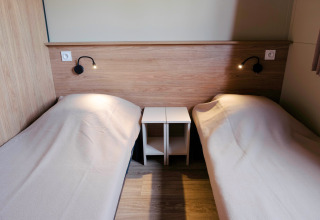 Zwei Einzelbetten mit Holzwandverkleidung im Chalet Portland bei Huttopia Calvados in der Normandie, Frankreich.