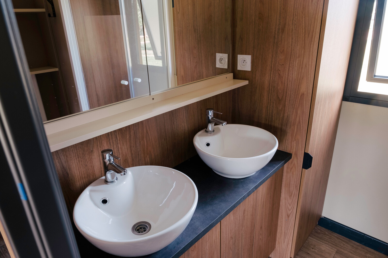 Moderne badkamer met twee ronde witte wastafels in Chalet Portland bij Huttopia Calvados, Normandië, Frankrijk.