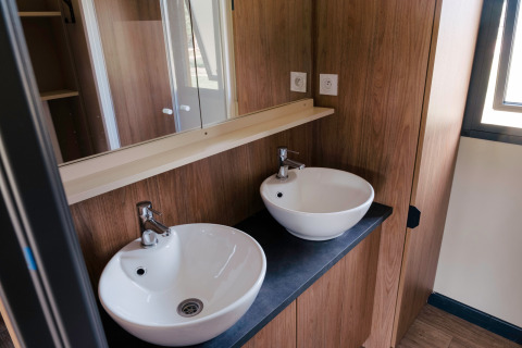 Modernes Badezimmer mit zwei runden weißen Waschbecken im Chalet Portland bei Huttopia Calvados in der Normandie.