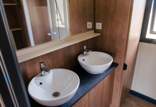 Modernes Badezimmer mit zwei runden weißen Waschbecken im Chalet Portland bei Huttopia Calvados in der Normandie.