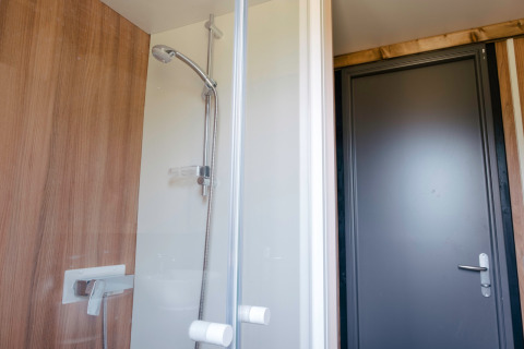 Moderne Duschkabine mit Holzwand und Glastür im Chalet Portland, Huttopia Calvados, Normandie, Frankreich.