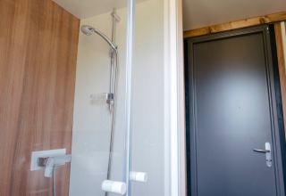 Moderne Duschkabine mit Holzwand und Glastür im Chalet Portland, Huttopia Calvados, Normandie, Frankreich.