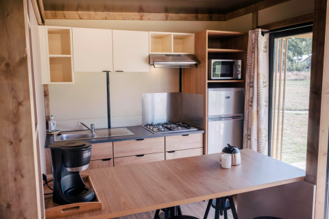 Moderne Küchenzeile im Chalet Portland, Huttopia Calvados - Normandie, mit Herd, Kühlschrank und Kaffeemaschine.
