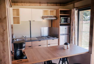 Moderne Küchenzeile im Chalet Portland, Huttopia Calvados - Normandie, mit Herd, Kühlschrank und Kaffeemaschine.