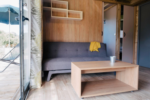 Stue i Chalet Portland på Huttopia Calvados - Normandie, med sofa, bord og åben dør til terrasse.