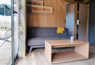 Stue i Chalet Portland på Huttopia Calvados - Normandie, med sofa, bord og åben dør til terrasse.