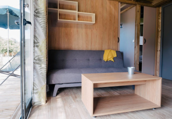 Stue i Chalet Portland på Huttopia Calvados - Normandie, med sofa, bord og åben dør til terrasse.
