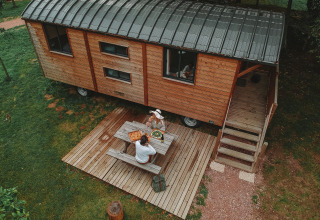 Vista aérea de una cabaña Roulotte de madera con terraza en Huttopia Calvados, Normandía, Francia, y dos personas comiendo.