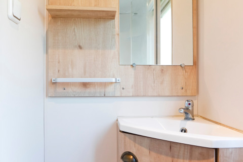 Helle Badezimmerecke in einer Hütte mit Waschbecken, Holzschrank, Spiegel und modernem Wasserhahn.