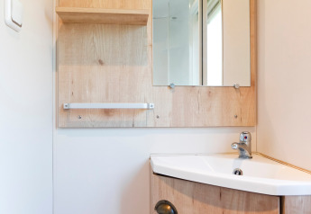 Coin salle de bain clair dans une cabane avec lavabo, meuble en bois, miroir, étagère et robinet moderne.