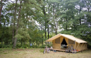 Tienda safari Toile & Bois Classic en Huttopia Lac de Sillé, Francia, rodeada de bosque y bicicletas fuera.