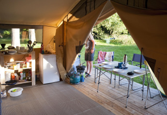 Vista interior de una tienda safari Toile & bois Classic en Huttopia Lac de Sillé, Francia, con equipo de camping.