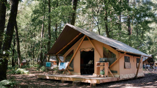 Tienda safari Bungalow tent Trappeur poêle en el bosque, con terraza de madera y sillas exteriores.
