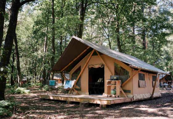 Tienda safari Bungalow tent Trappeur poêle en el bosque, con terraza de madera y sillas exteriores.