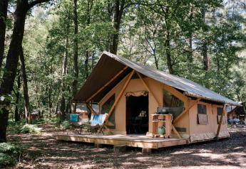 Safaritent Bungalow tent Trappeur poêle in een bos, met houten veranda en buitenstoelen op het terras.