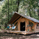 Tienda safari Bungalow tent Trappeur poêle en el bosque, con terraza de madera y sillas exteriores.