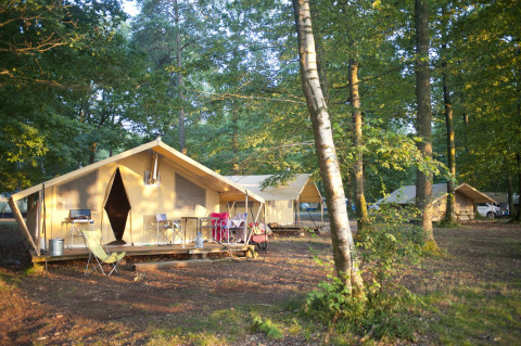 Tienda safari Bungalow Trappeur poêle en Huttopia Lac de Sillé, Francia, rodeada de árboles y naturaleza.