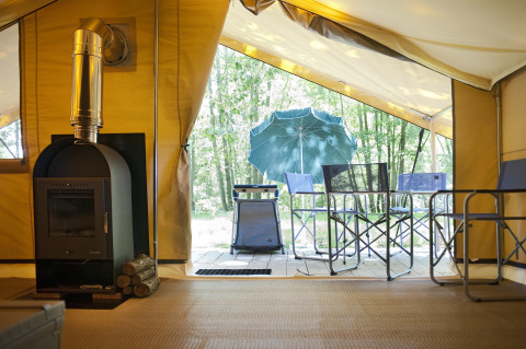 Blik uit de safaritent Bungalow Trappeur poêle bij Huttopia Lac de Sillé met houtkachel en terrasstoelen.